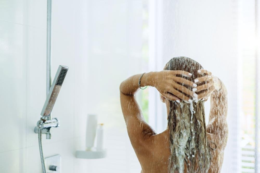 Back view of woman taking shower in modern white bathroom in the morning. Daily routine lifestyle photo.