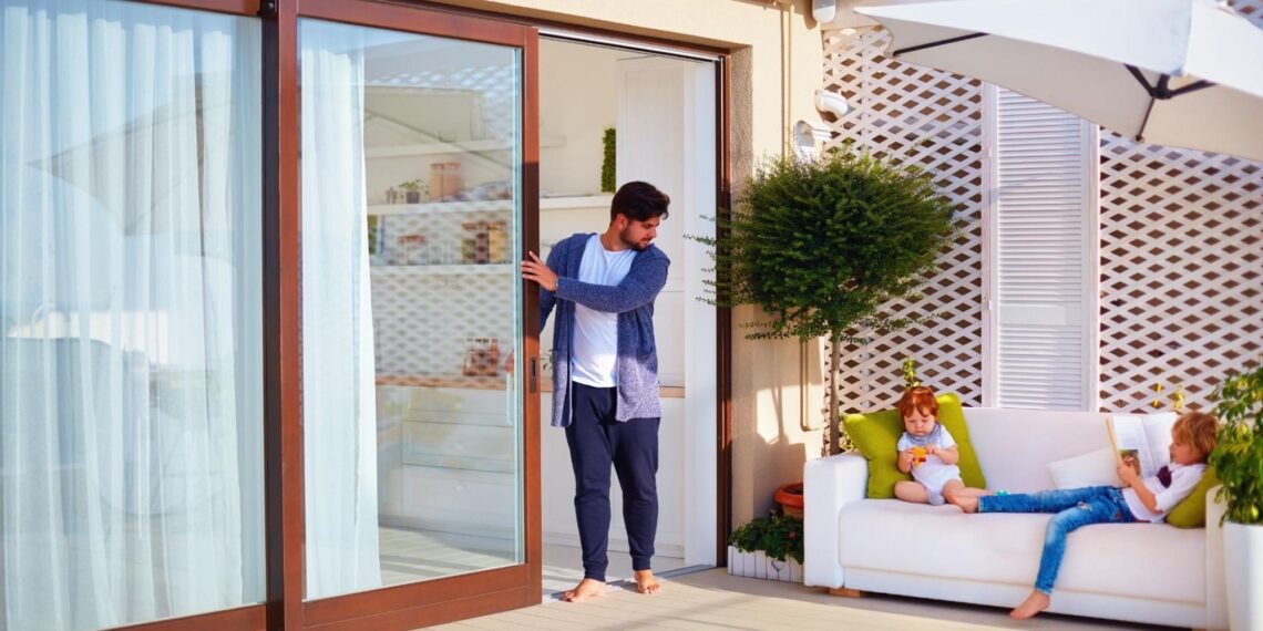 A man opening a sliding glass door to access a patio area.