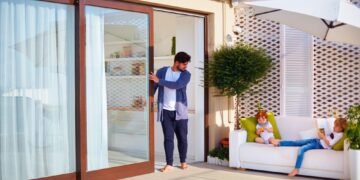 A man opening a sliding glass door to access a patio area.