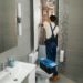A man wearing overalls works on fixing a toilet, surrounded by plumbing tools and parts.