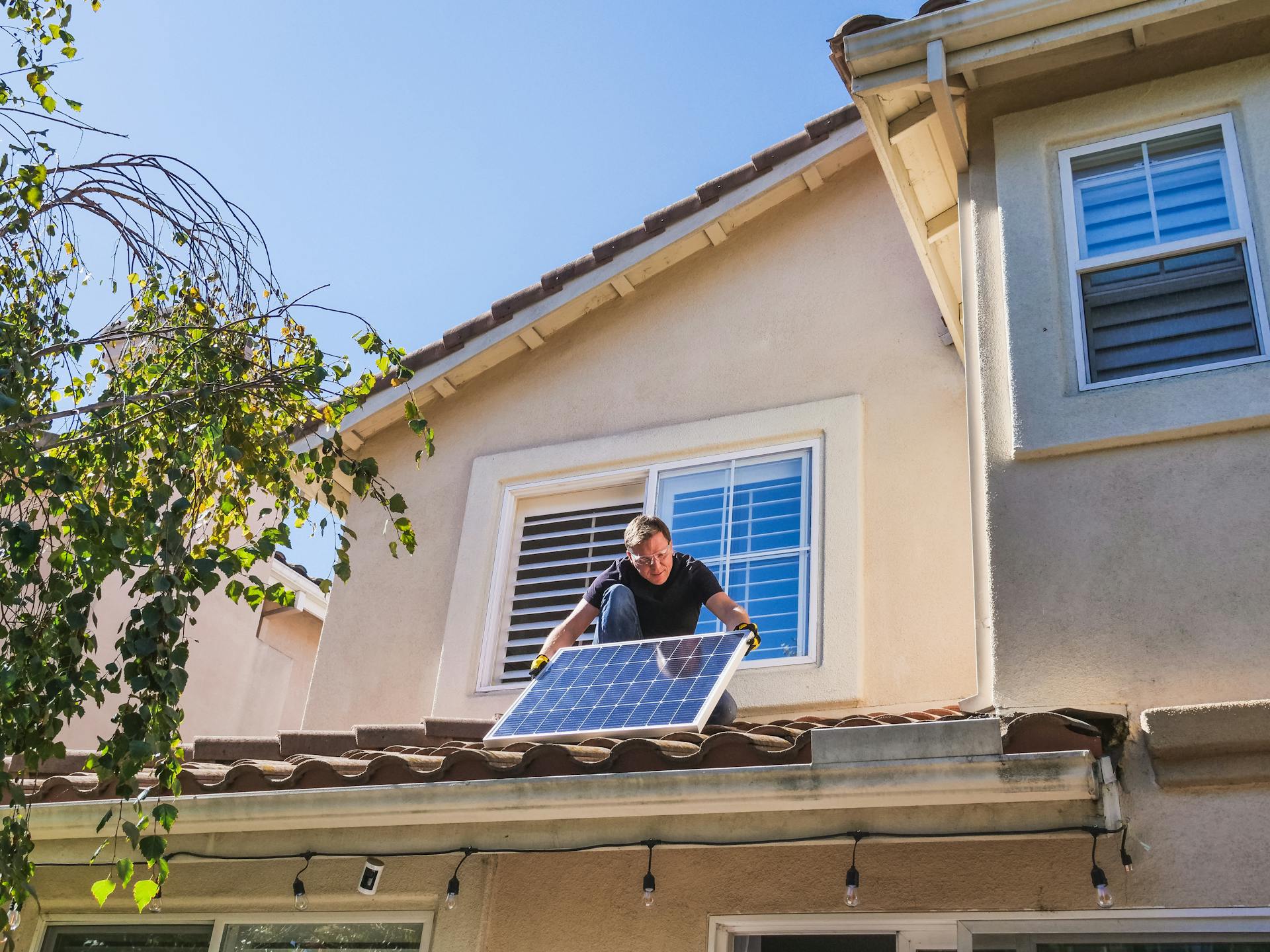 A man installs a solar panel on a rooftop, demonstrating renewable energy efforts for residential use.